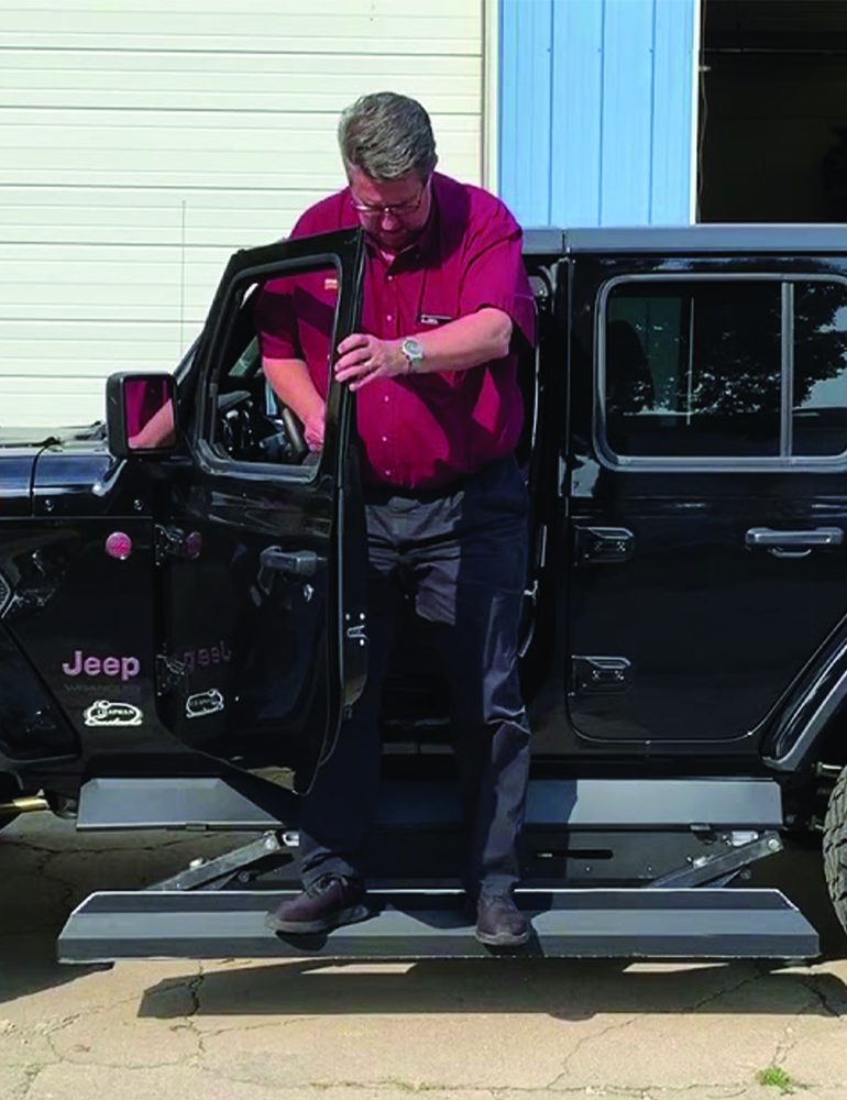 Driver testing electric running boards on a black Jeep Rubicon